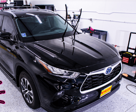 Black Toyota Highlander being worked on in a shop; the hood is wet.