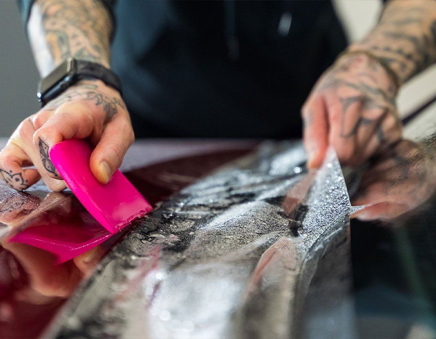 A man with tattoos is wrapping a car with a pink spatula.