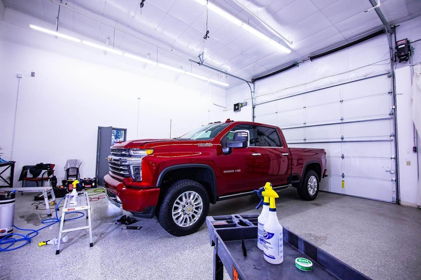 Red pickup truck inside a garage; tools and supplies are nearby. Garage door is open.