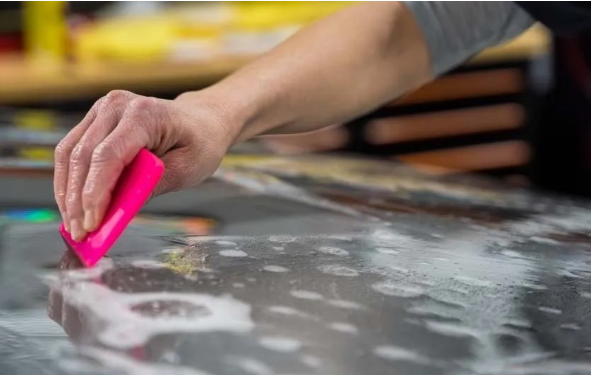 Person using a pink squeegee to apply film with soapy water.