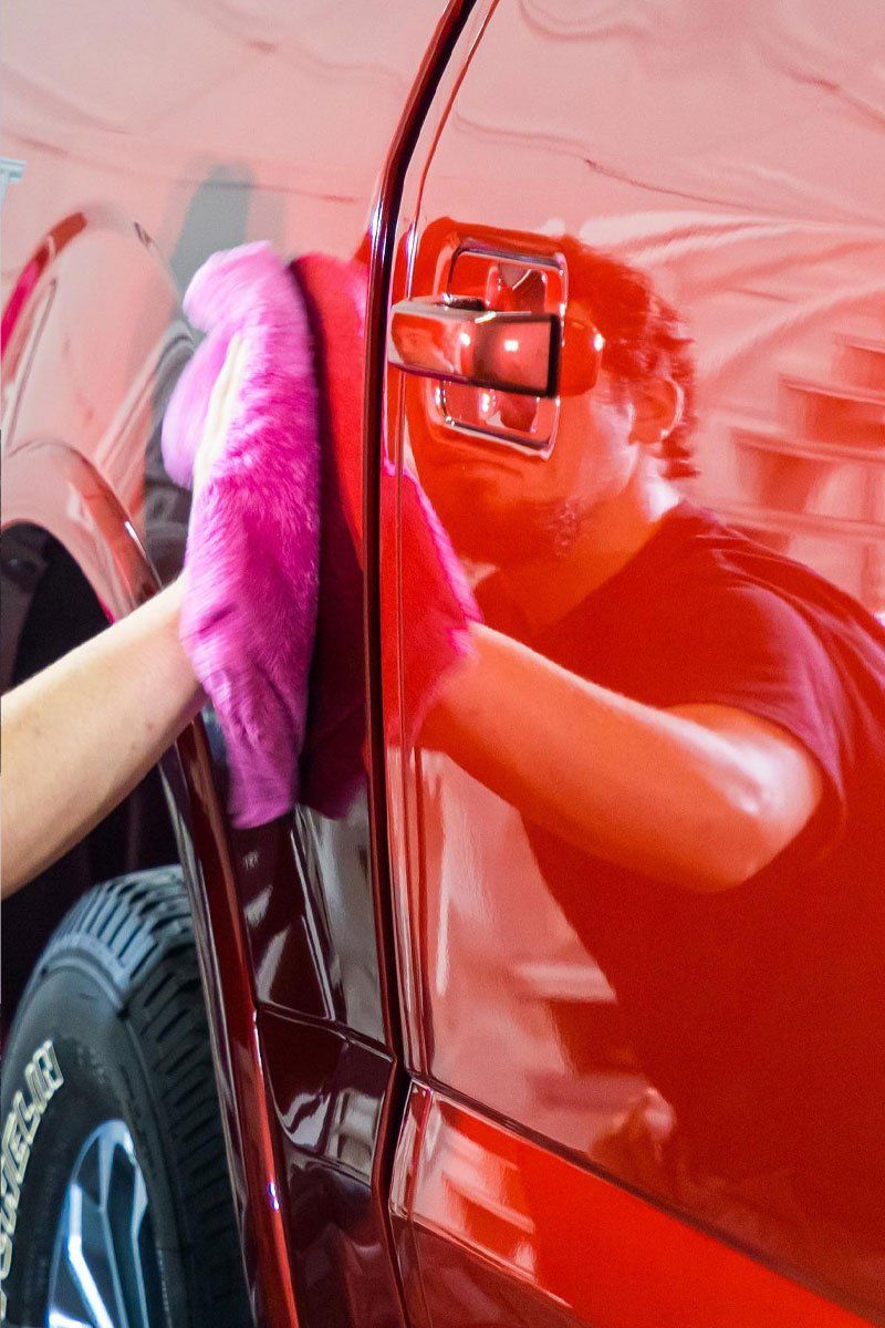Person polishing a shiny red car with a pink microfiber cloth.