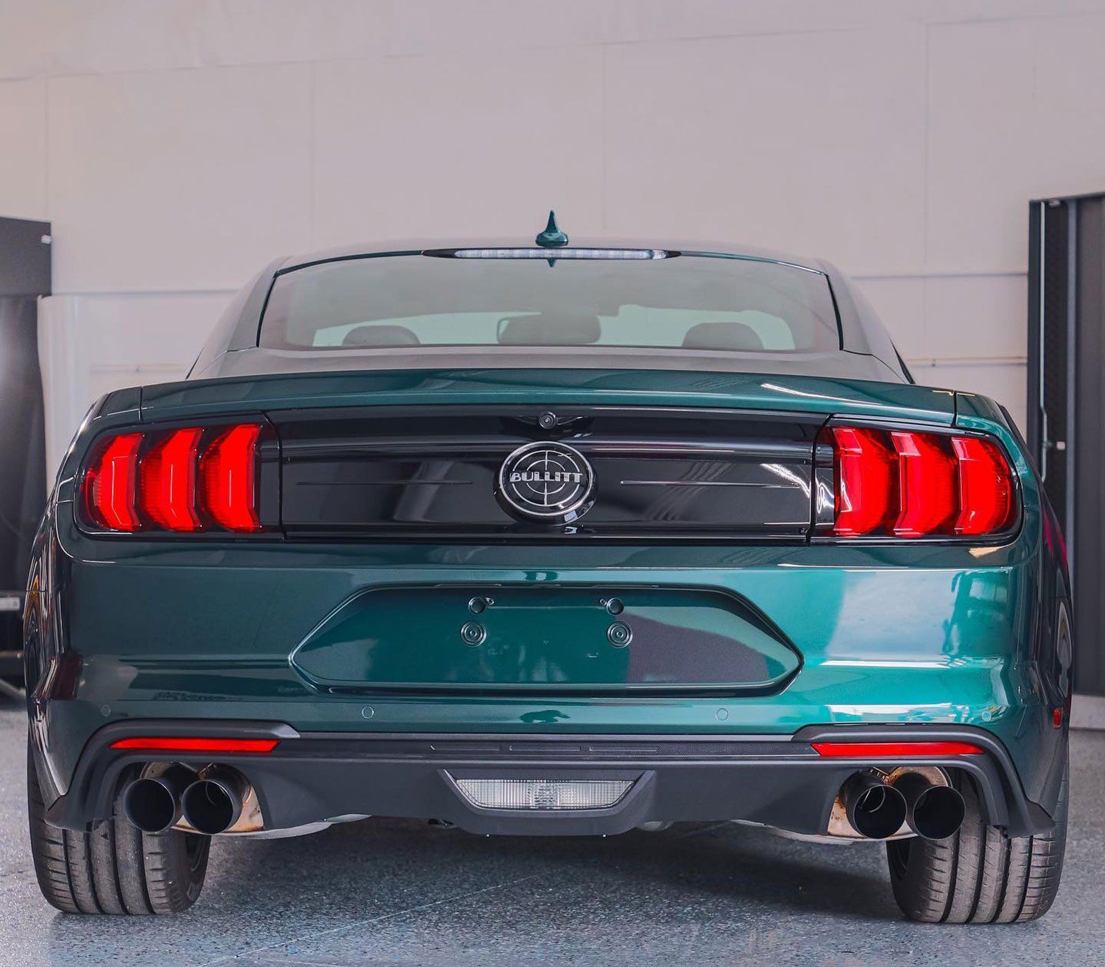 Green Ford Mustang rear view with black trim, red taillights, and quad exhaust.