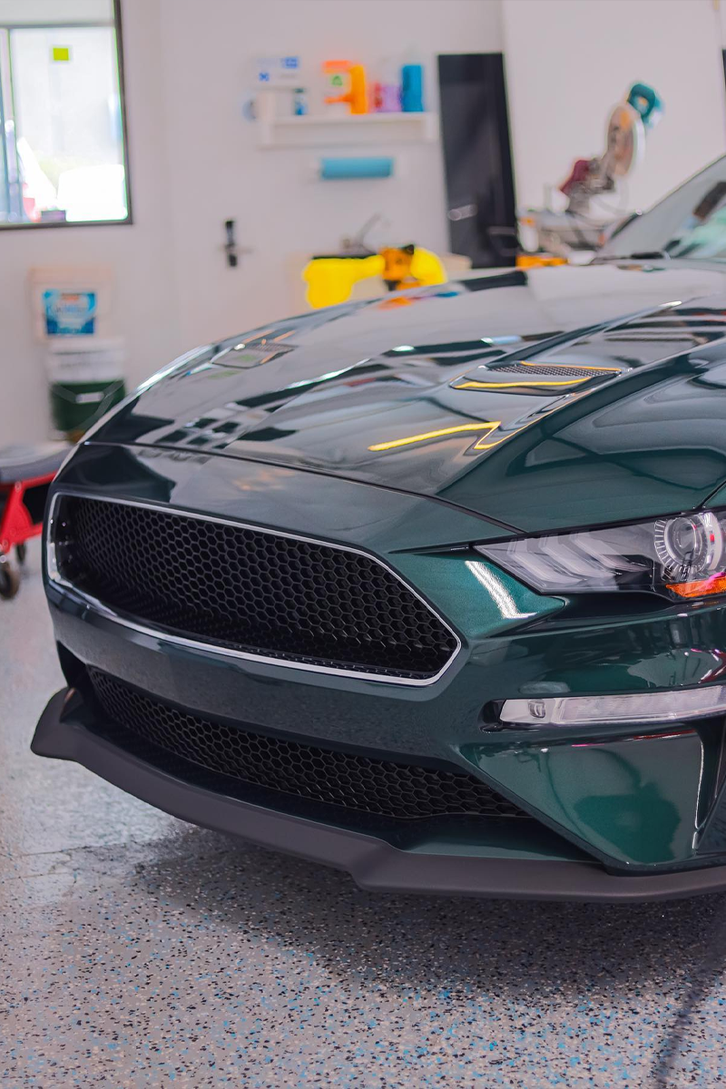 Dark green Ford Mustang front view in a well-lit garage, glossy paint, black grill.