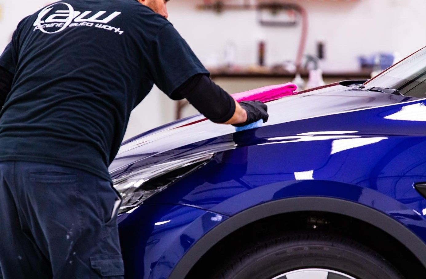 Person applying a product to the hood of a blue car. They are wearing gloves and a dark shirt.