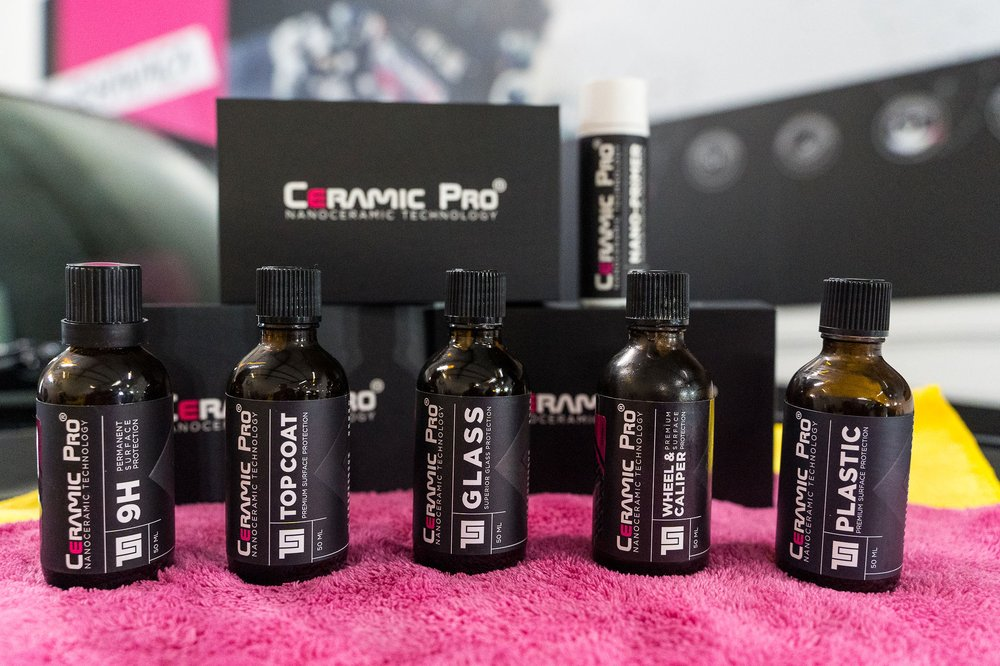 Ceramic Pro car care products: bottles on a pink cloth, black boxes in the background.