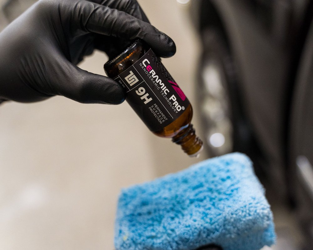 Gloved hand dispensing Ceramic Pro 9H coating onto a blue applicator pad.