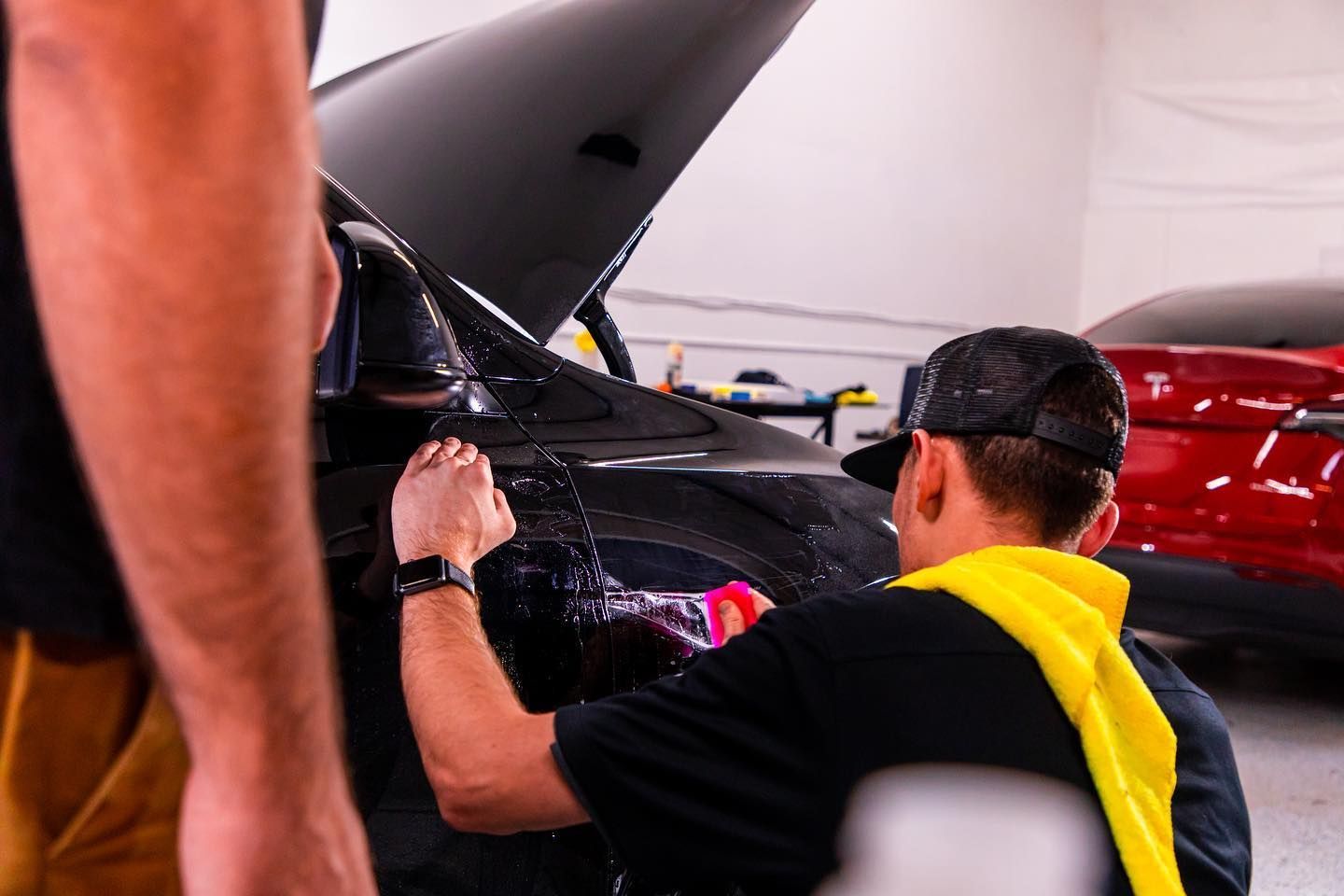 Two people working on a black car in a garage. One sprays water.