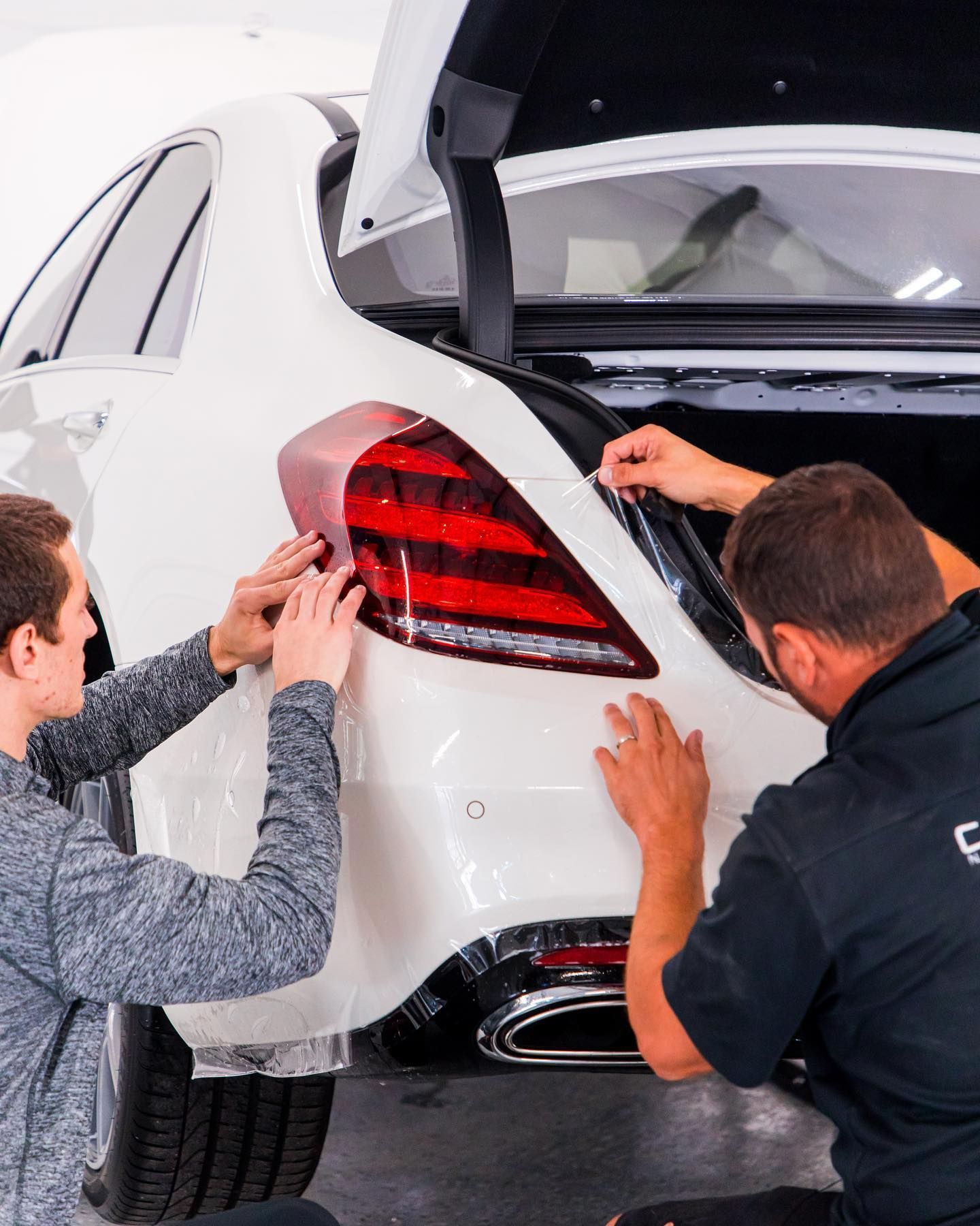 Two men applying film to the taillight of a white car in a garage.
