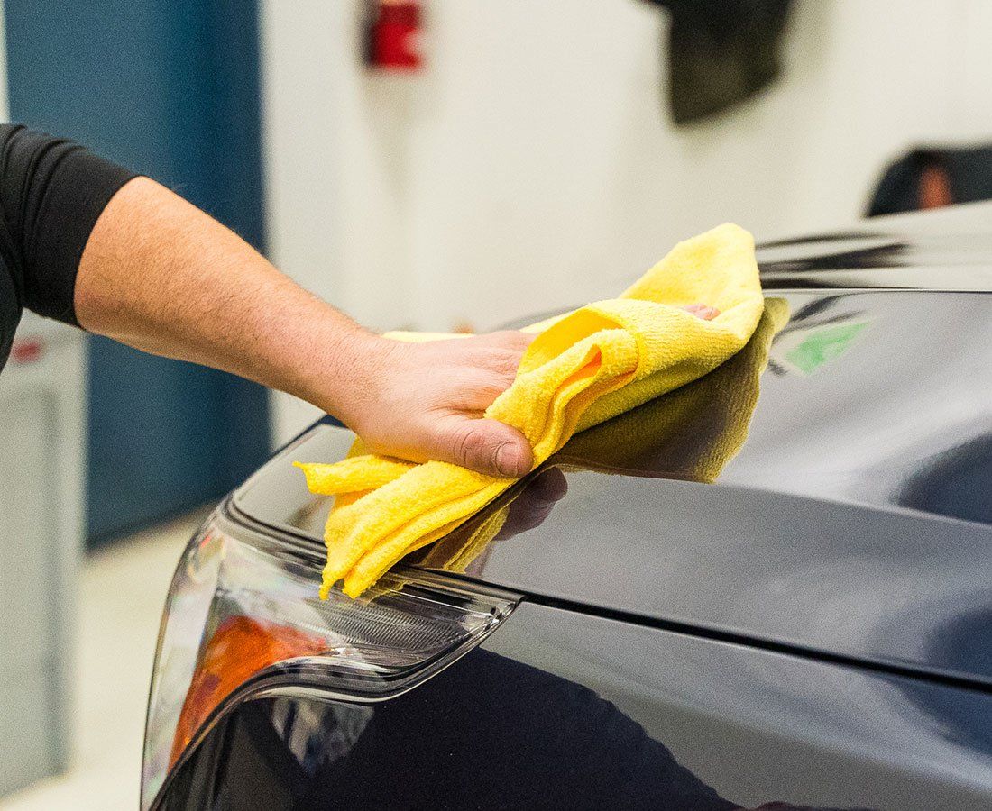Person wiping down a dark car with a yellow microfiber cloth.