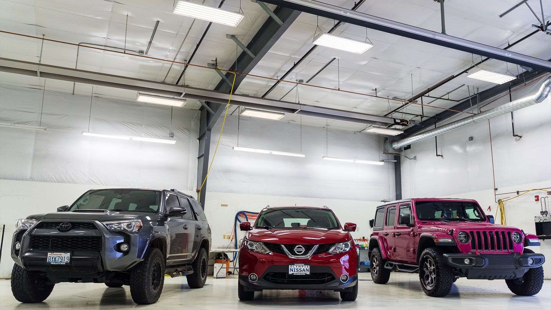 Three SUVs parked inside a well-lit garage: gray Toyota, red Nissan, and pink Jeep.