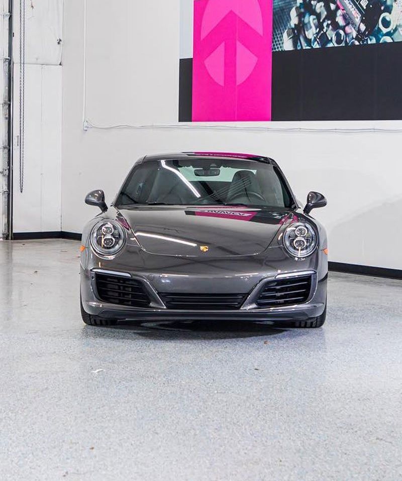Gray Porsche 911 car parked inside a garage with a pink peace sign on the wall.