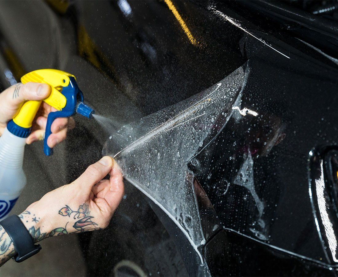 Person spraying liquid on car while applying protective film.