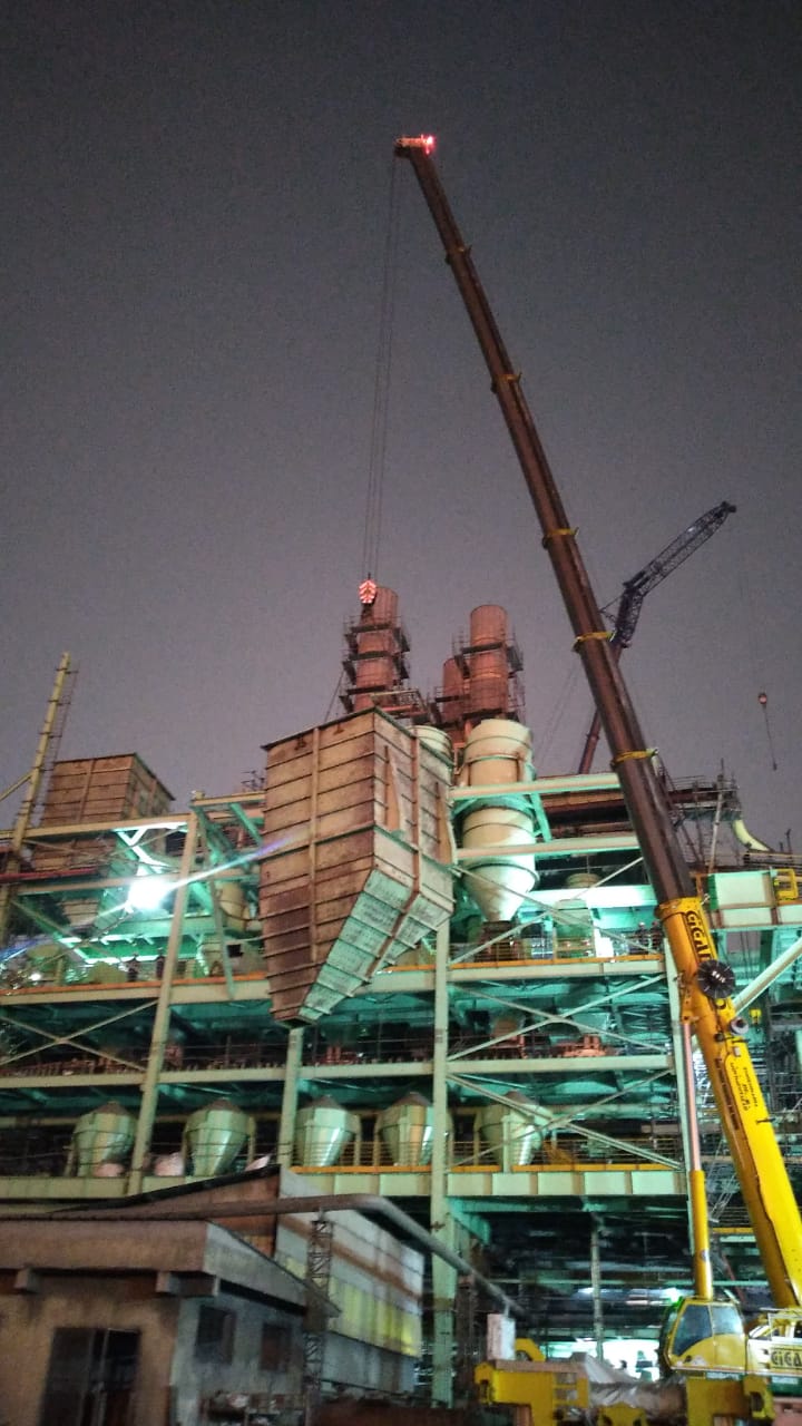 Um grande guindaste está levantando uma grande estrutura em uma fábrica à noite.