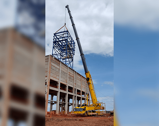 Um grande guindaste amarelo está levantando uma estrutura de metal no topo de um edifício.