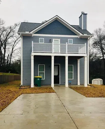 A blue house with a balcony and a green trash can in front of it.