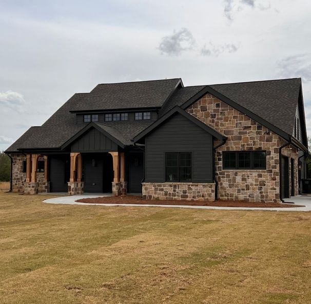 A large house with a black roof is sitting in the middle of a grassy field.