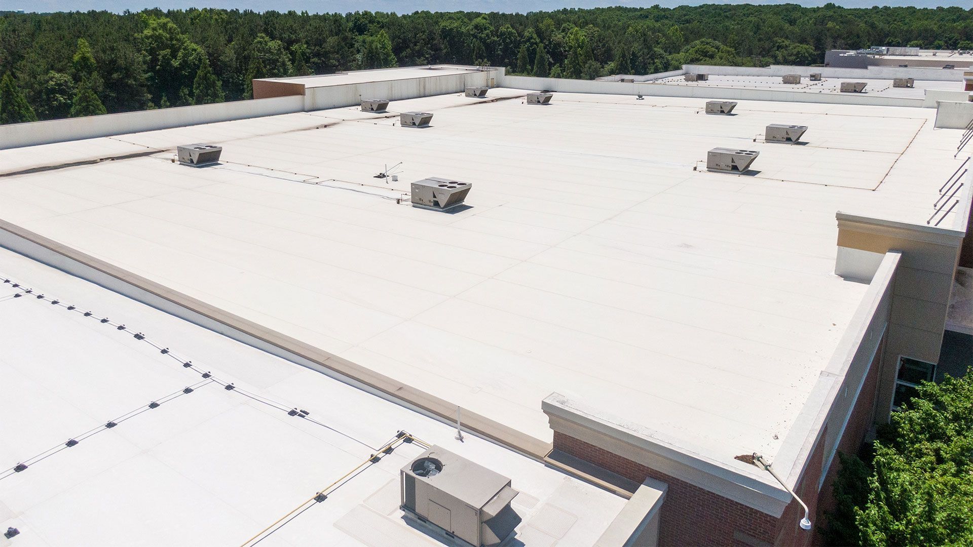 The roof of a large building with a white roof and trees in the background.