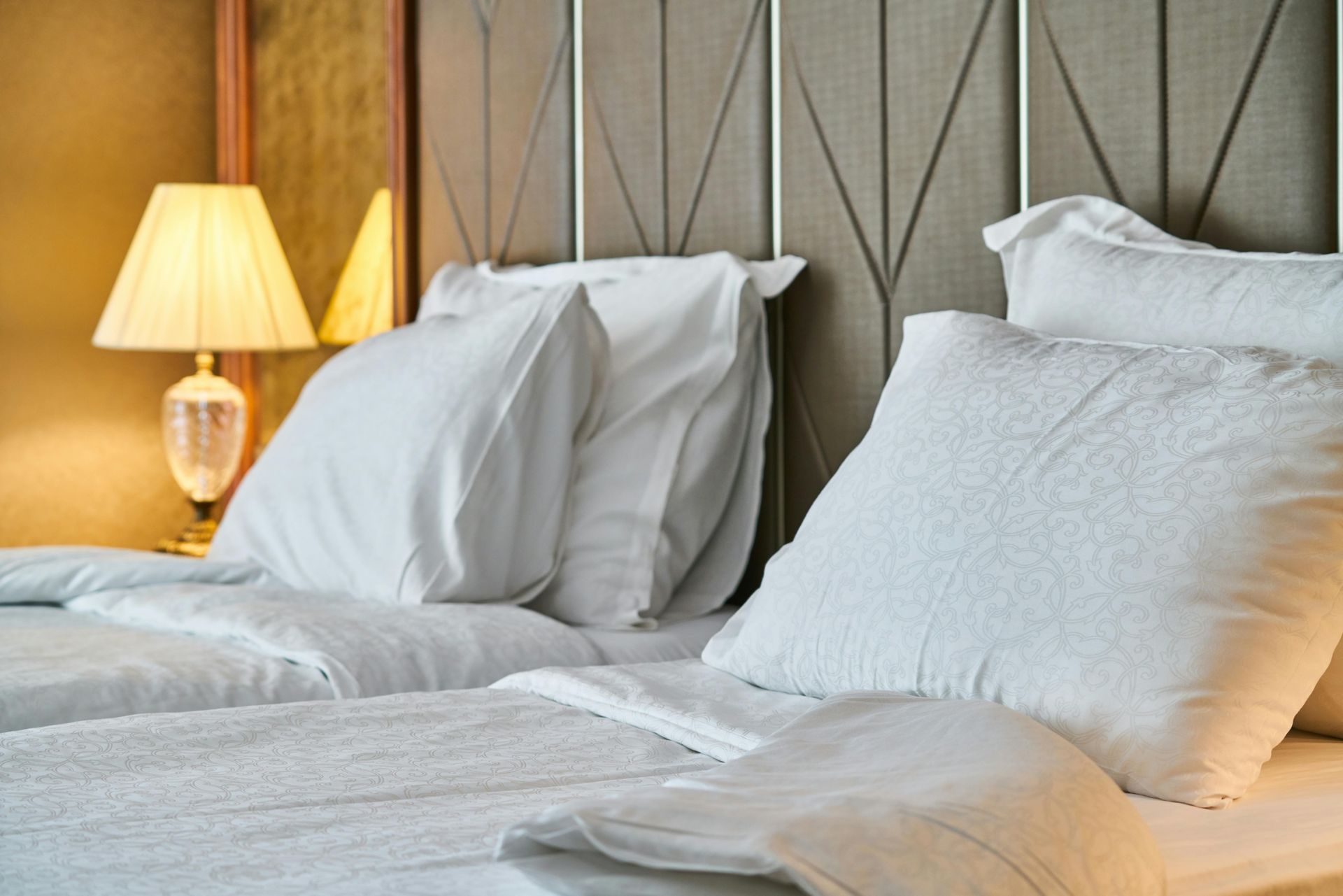There are two beds in the room with white sheets and pillows.