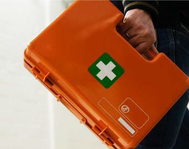 Kit di pronto soccorso arancione con una croce verde, trasportato a mano