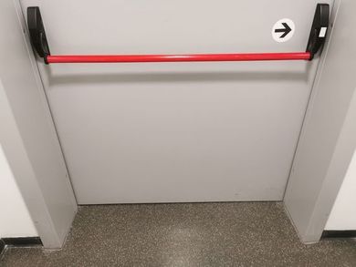 Barra di sostegno rossa all’ingresso di un bagno accessibile, con pavimento grigio e pareti bianche