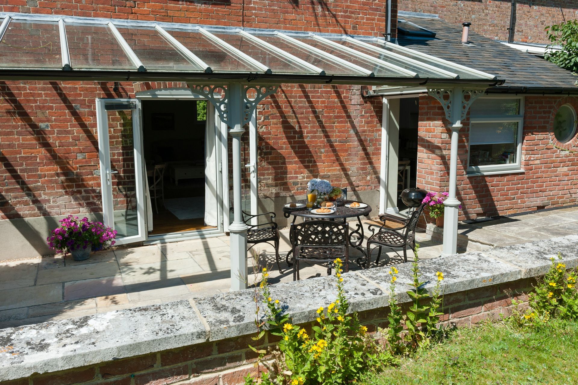 Patio with metal table and chairs beside a brick house and covered porch.