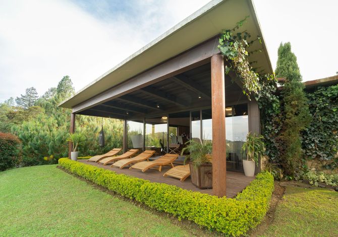Open-air garden pavilion with wooden lounge chairs, green lawn, and lush landscaping