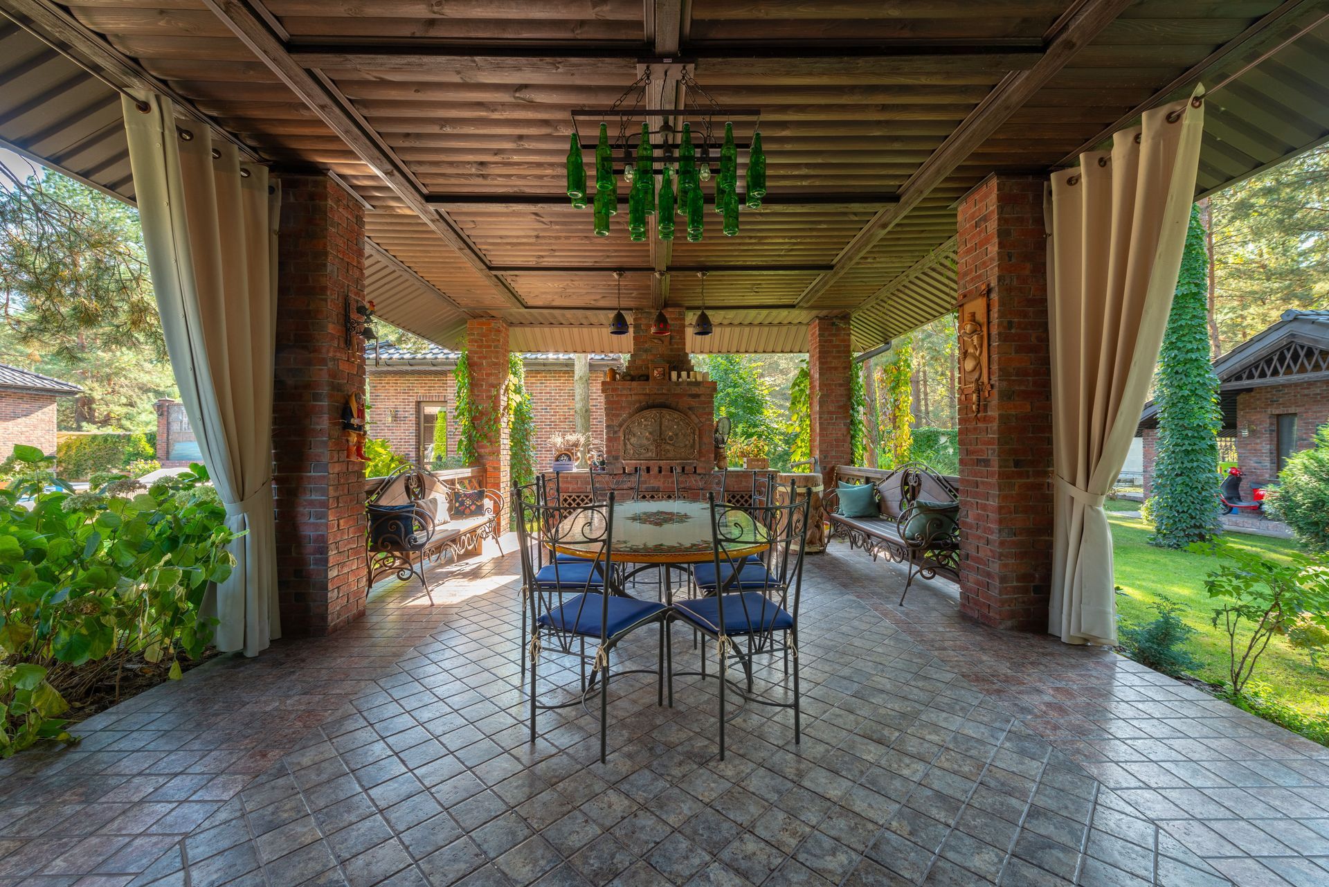 Covered patio with a tiled floor, hanging green planter, and a small table and chairs overlooking a garden