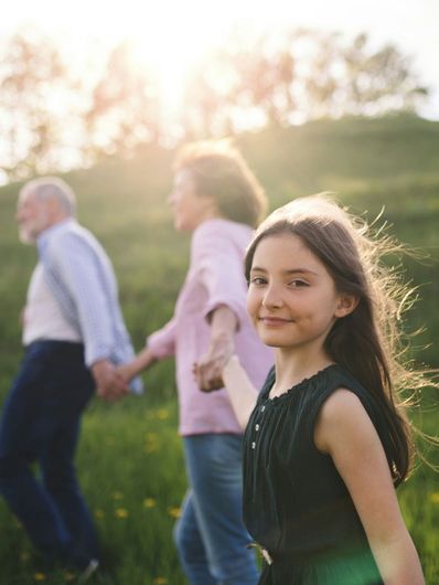 A little girl is holding the hand of her grandparents while walking in a field.