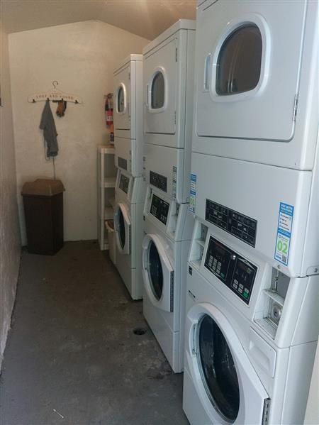 Laundry room with several stacked washer and dryer units. A trash can and wall hooks are visible.