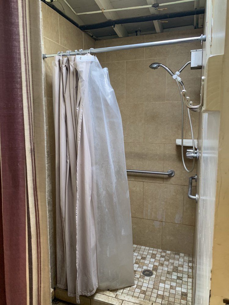 Shower stall with beige tile, shower curtain, and a grab bar.