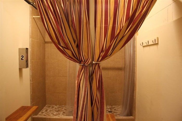 Shower stall with striped curtain tied in the middle, tile floor, and hooks on wall.
