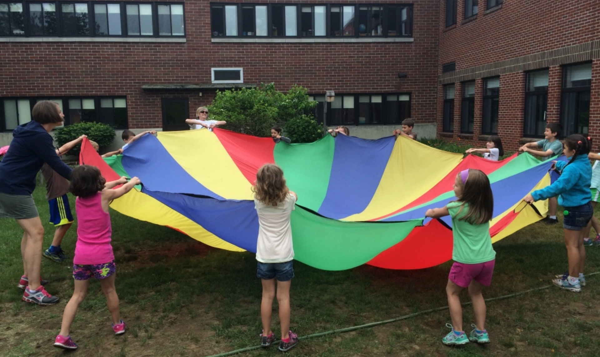 Children holding a colorful parachute outdoors in a school courtyard