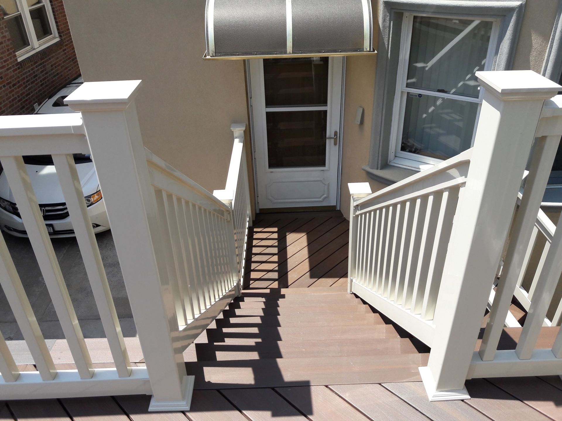 A set of wooden stairs with white railings leading down to a residential entryway with a door and metal awning.