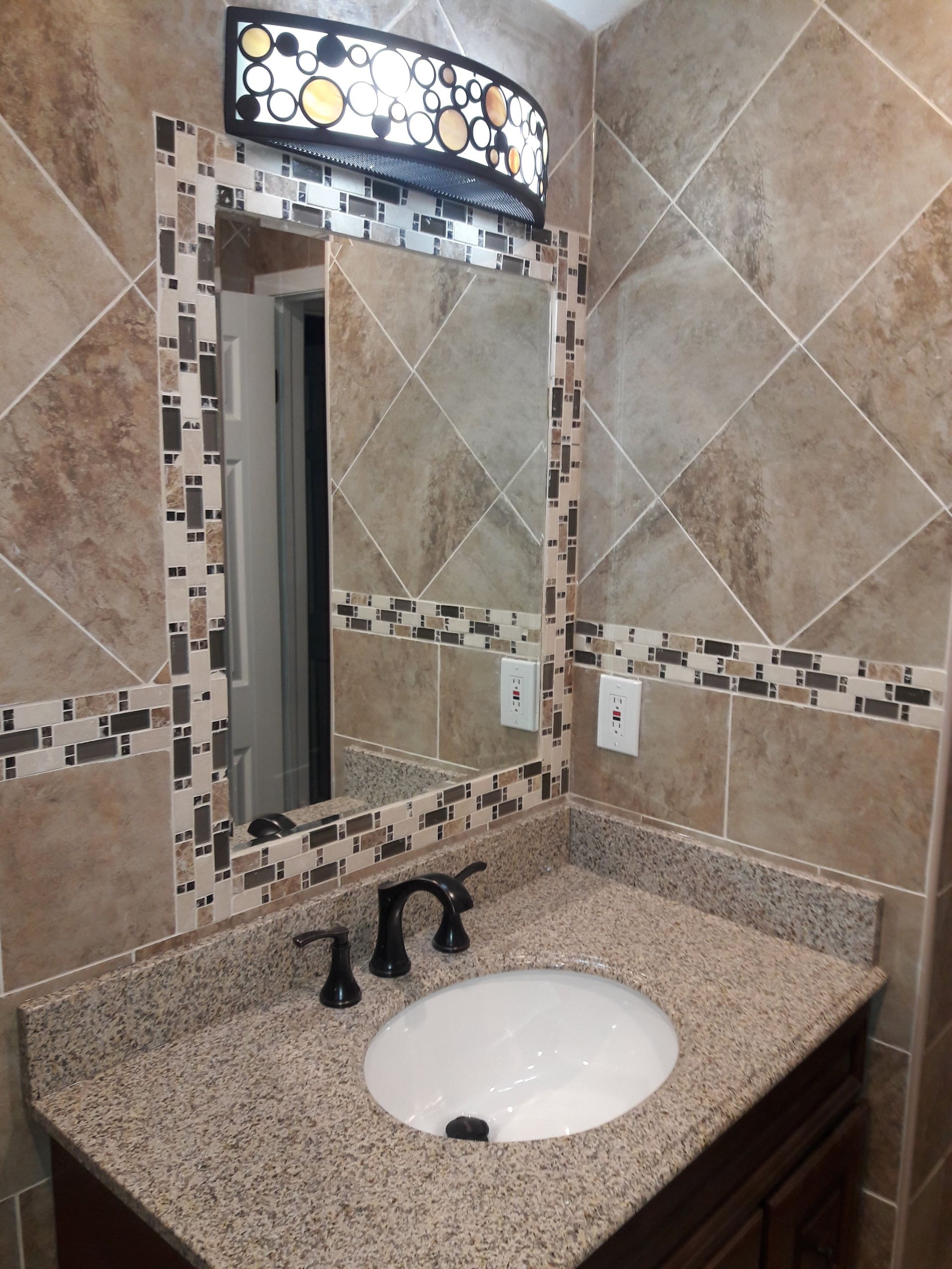 A bathroom vanity with a speckled granite countertop, white sink, oil-rubbed bronze faucet, and tiled wall with a mirror.