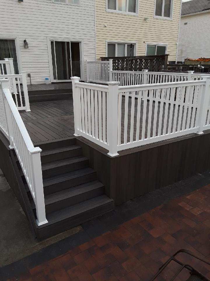 An elevated dark brown composite deck with white railings and stairs leading down to a paved patio behind a home.