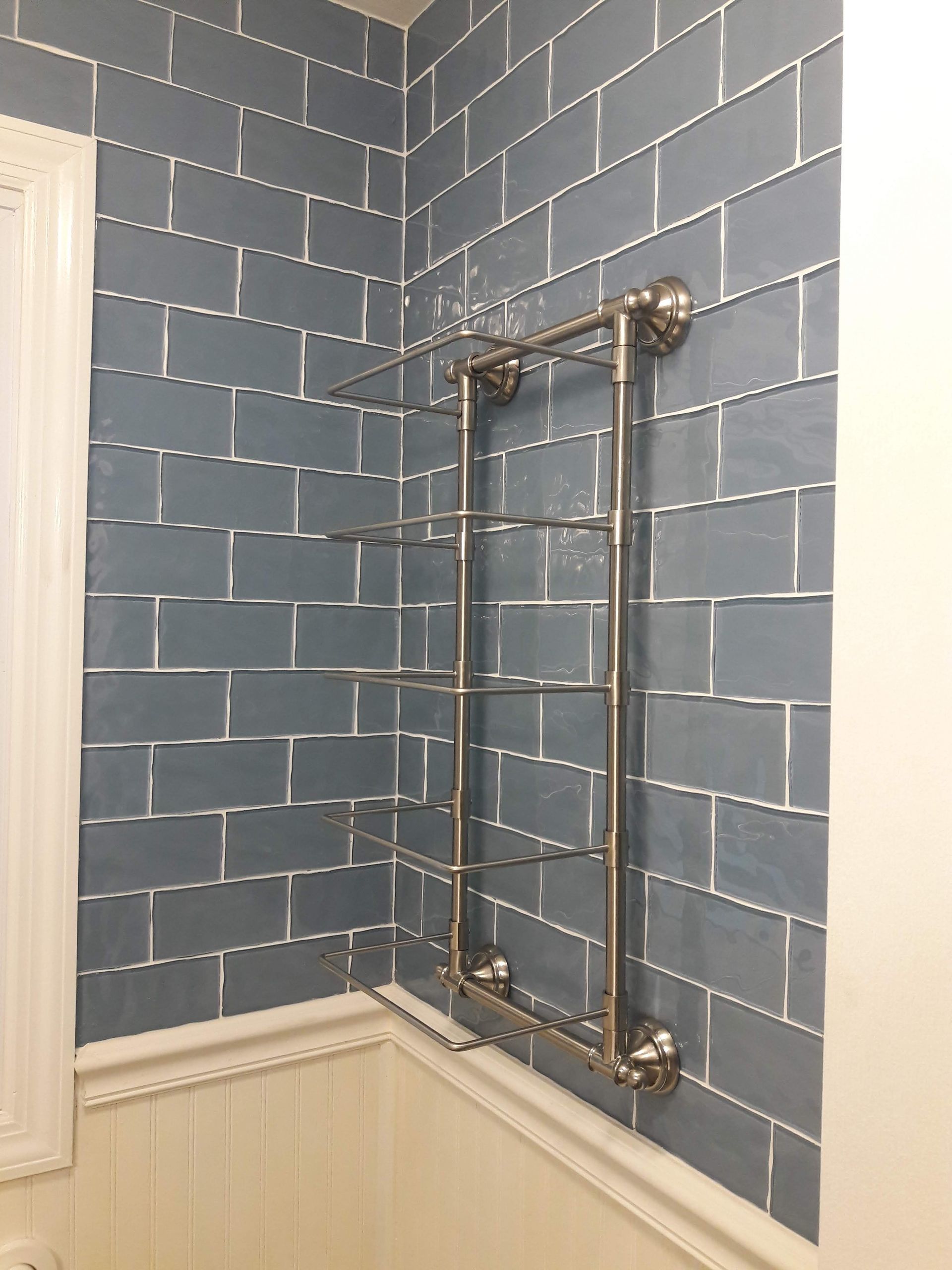 A metal multi-tier towel rack mounted on a wall featuring blue subway tiles and white wainscoting.