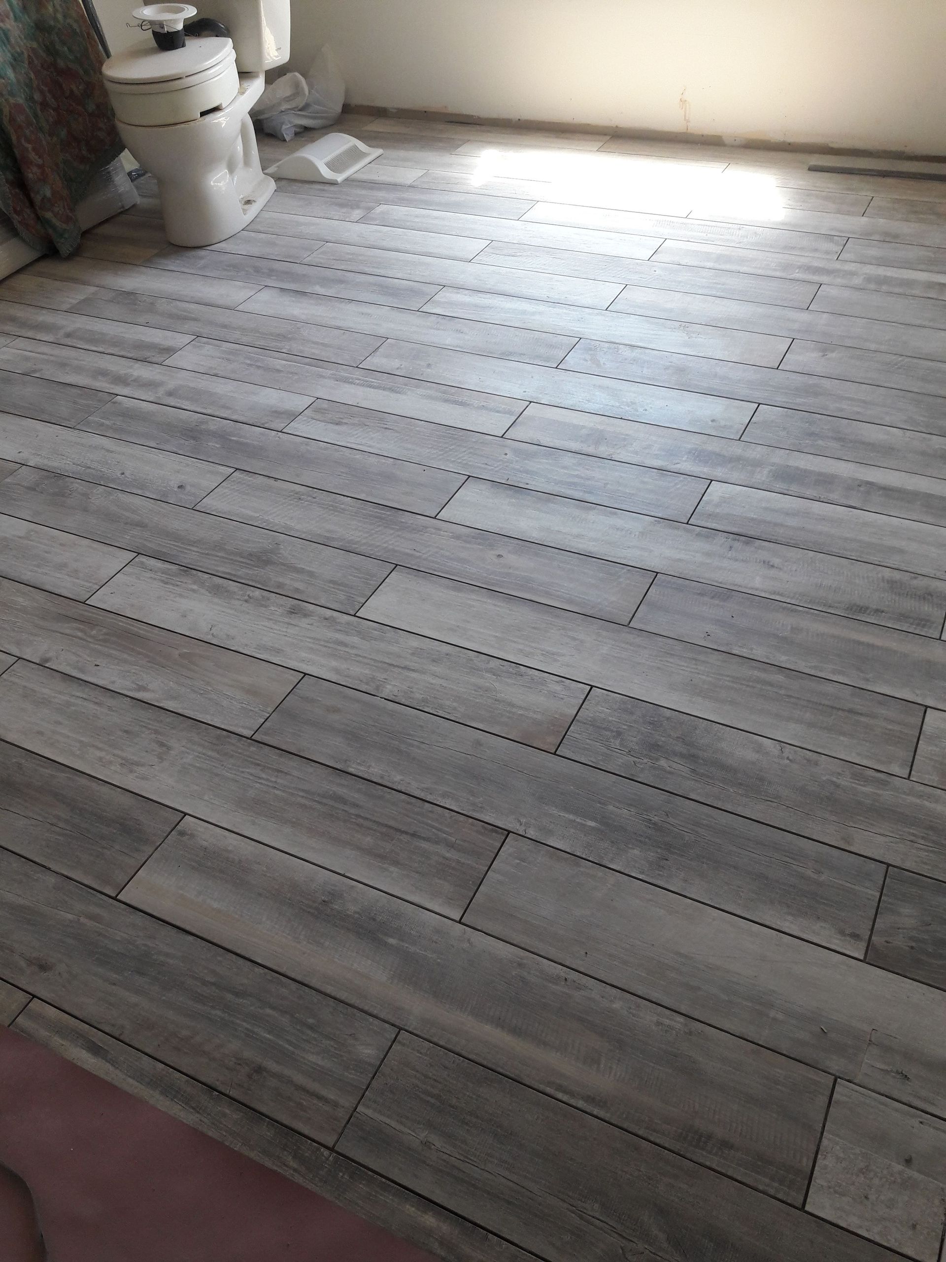 Newly installed gray wood-look luxury vinyl plank flooring in a bathroom, surrounding a toilet base.
