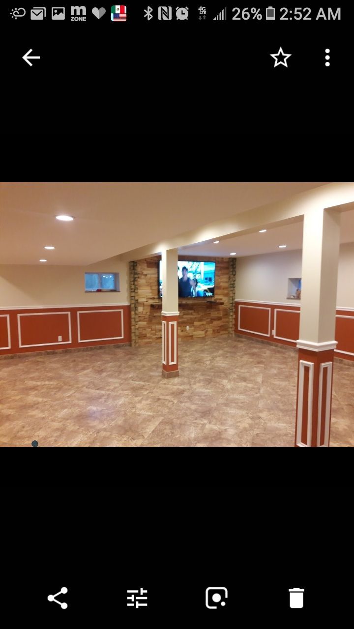 A finished basement featuring a stone fireplace with a mounted TV, support columns, and red wainscoting on the walls.