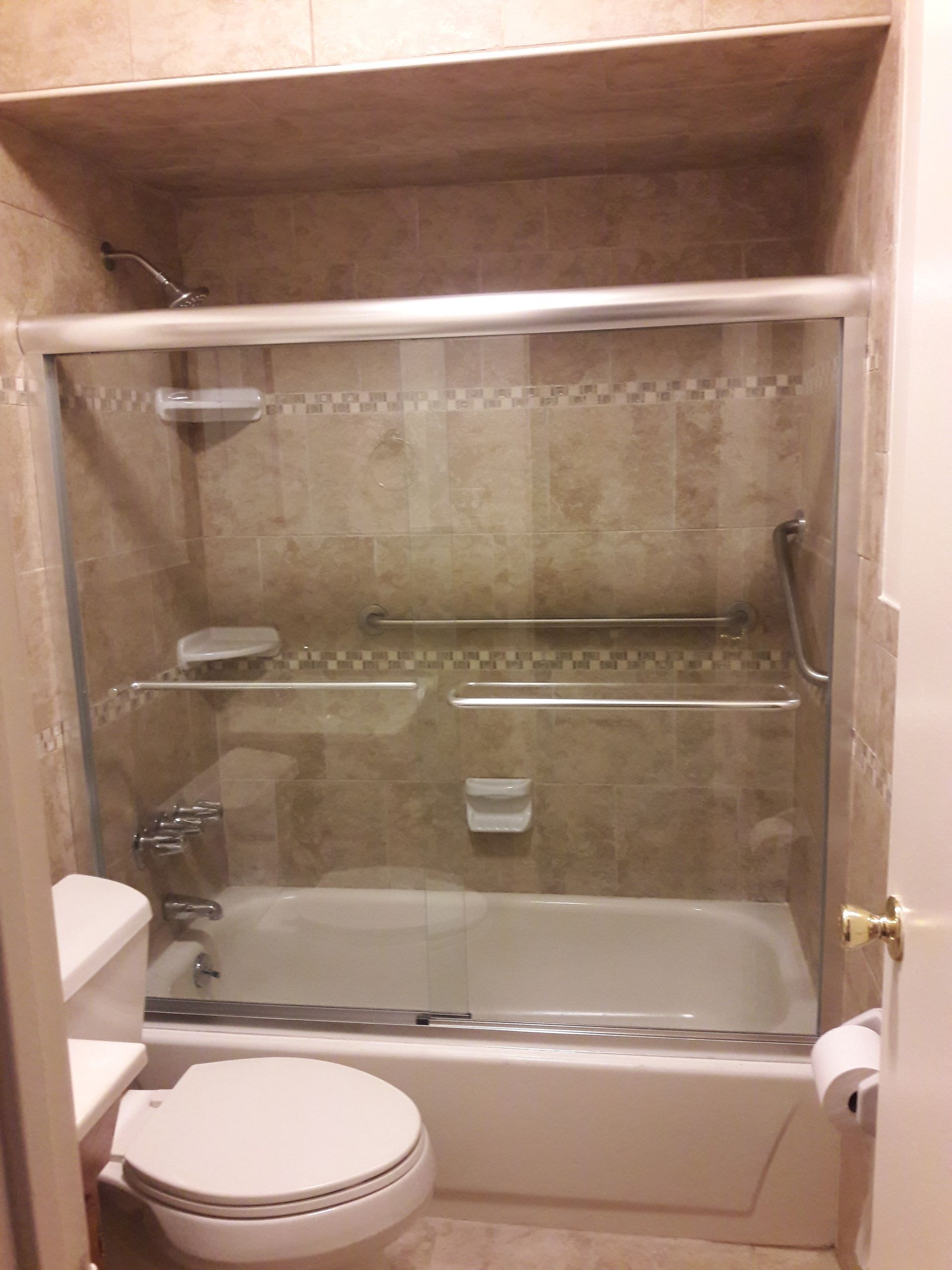 A neutral-toned bathroom featuring a white toilet next to a beige-tiled bathtub with a glass sliding shower door.
