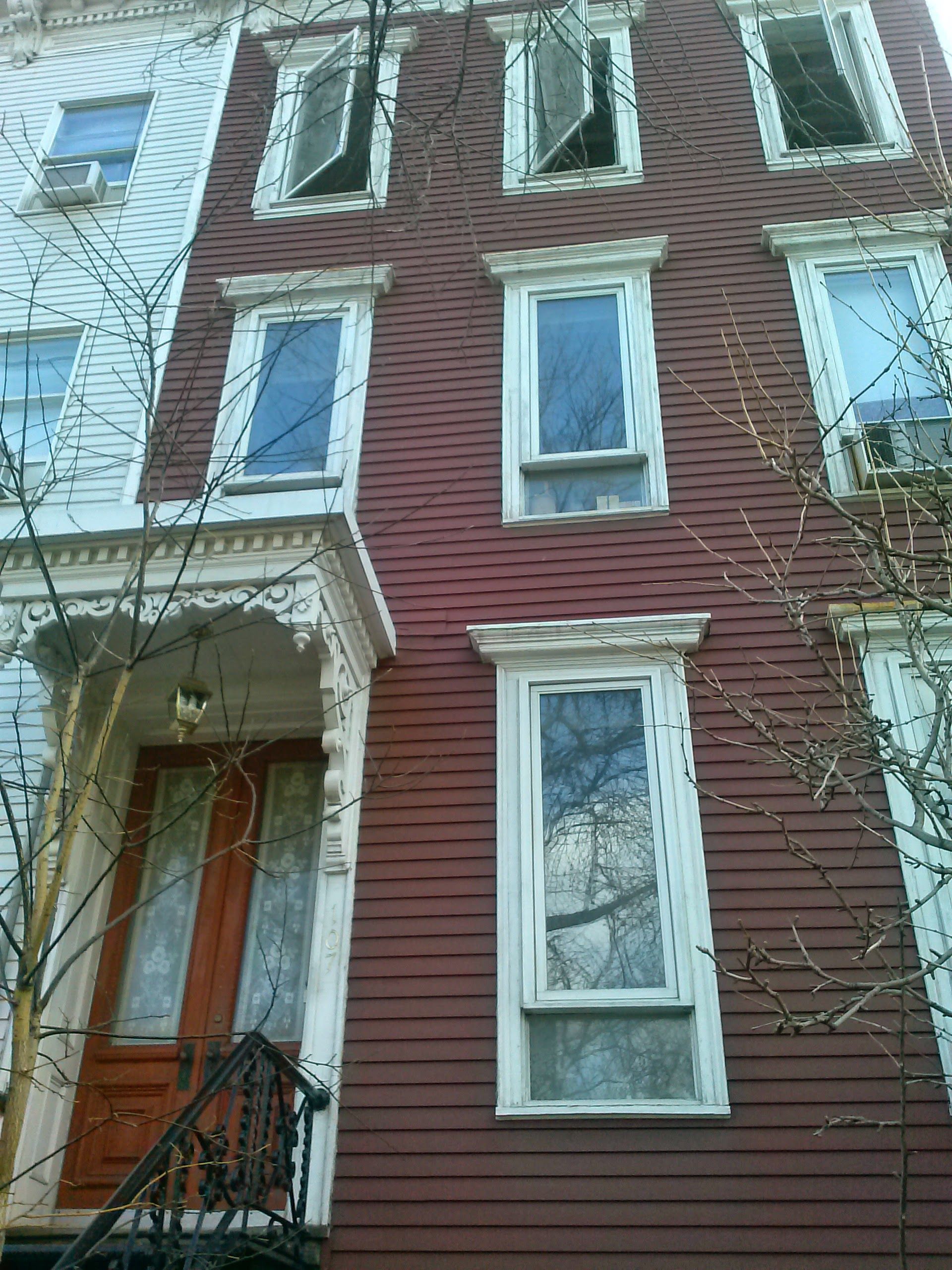 A red-sided townhouse exterior featuring a wooden front door, ornate porch details, and tall, rectangular windows.