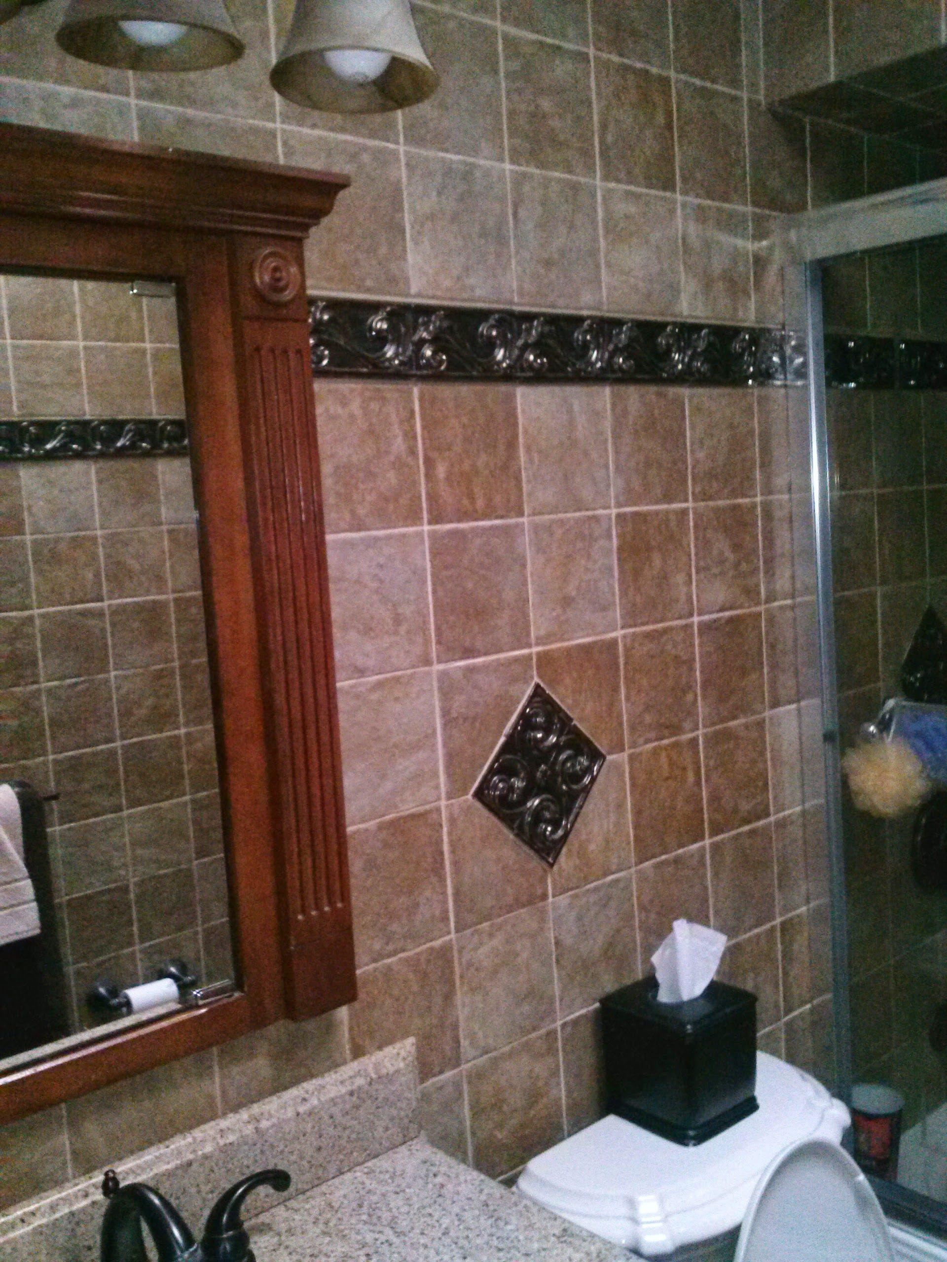 A bathroom vanity area with brown tiled walls, a wooden mirror frame, a black tissue box, and a toilet.