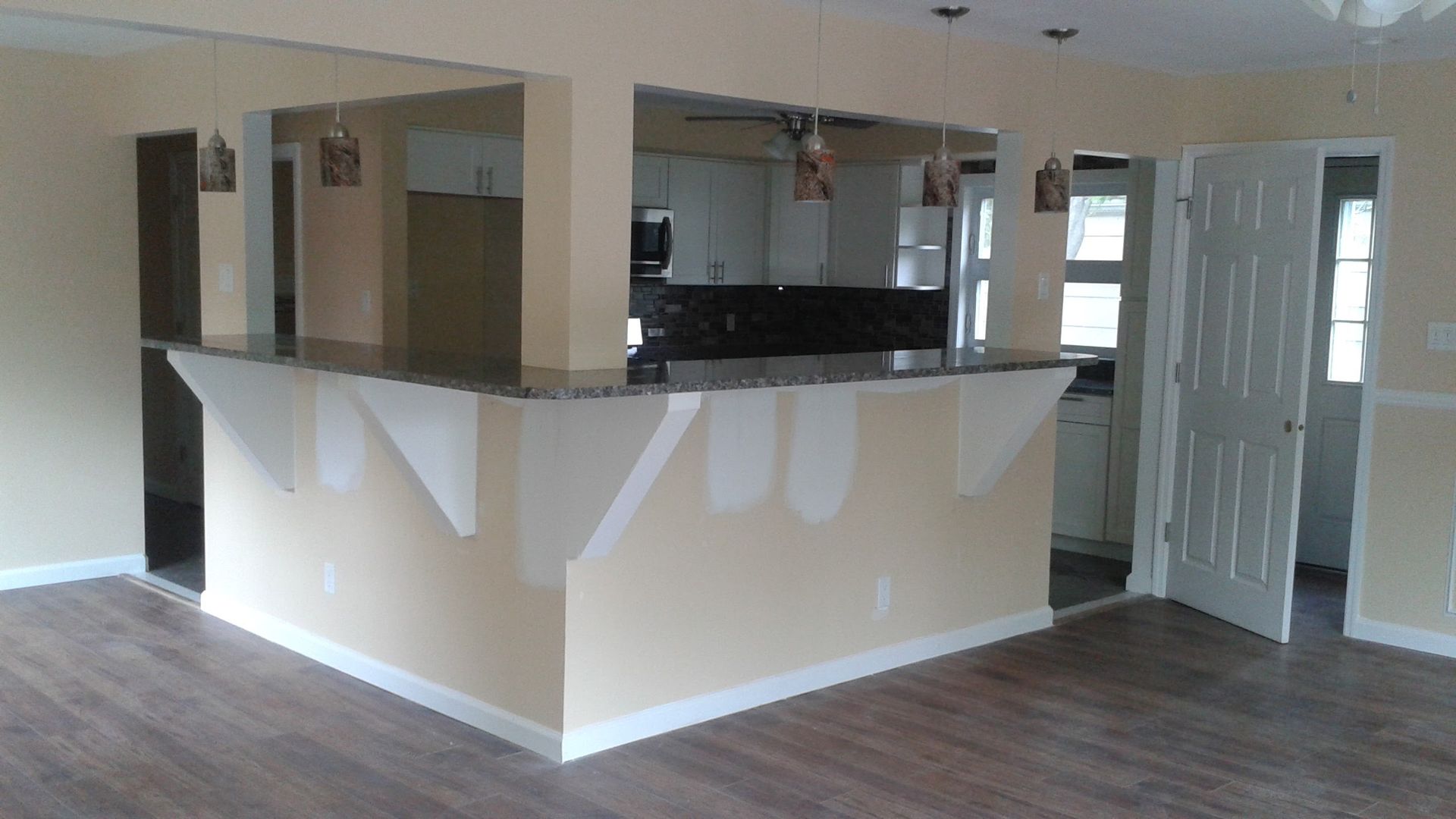 A kitchen counter island with unfinished drywall patches in a room with light beige walls and dark wood-look flooring.