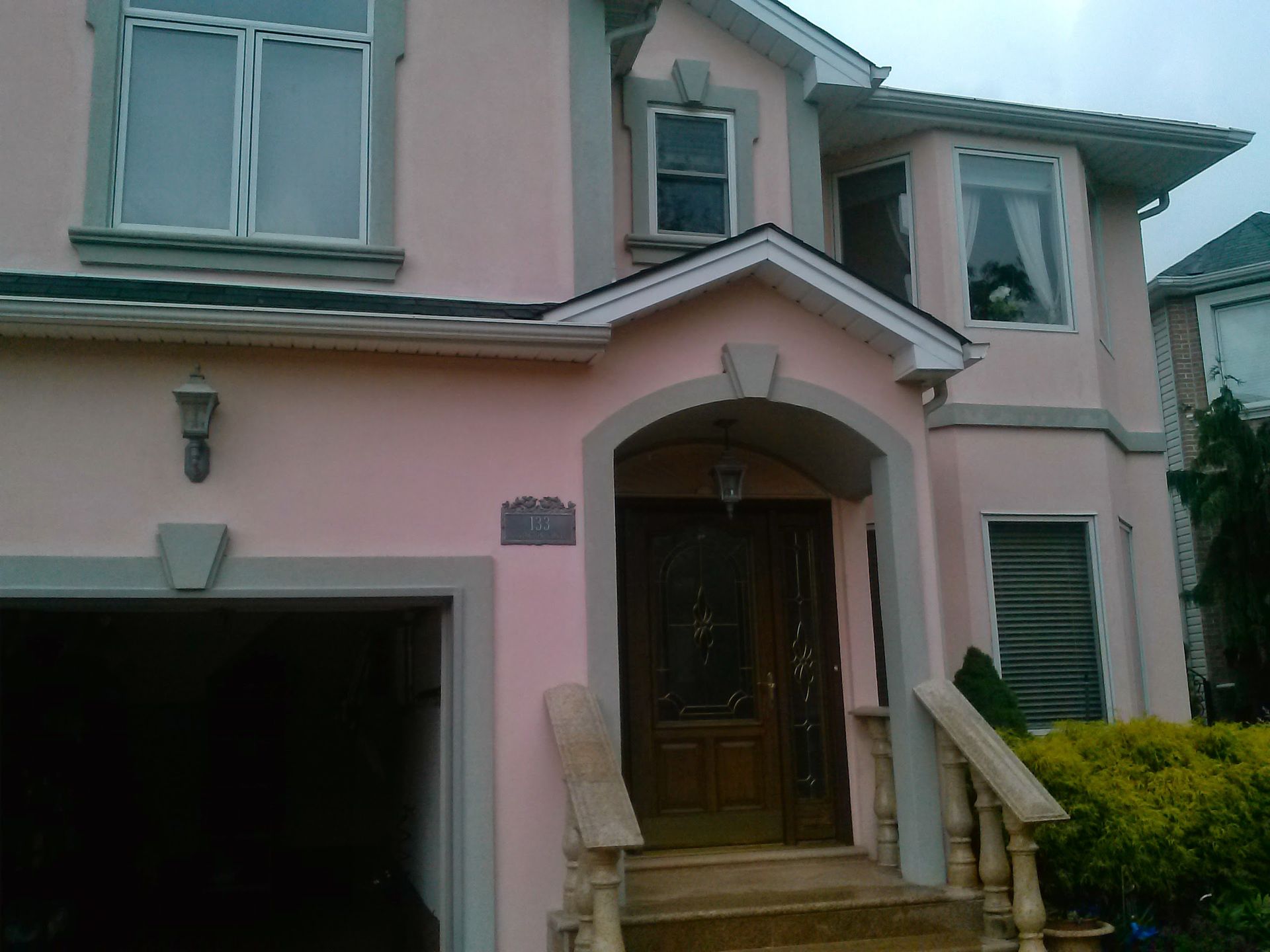 A two-story house with pastel pink exterior walls, grey trim, an arched front entryway, and a garage on the lower level.