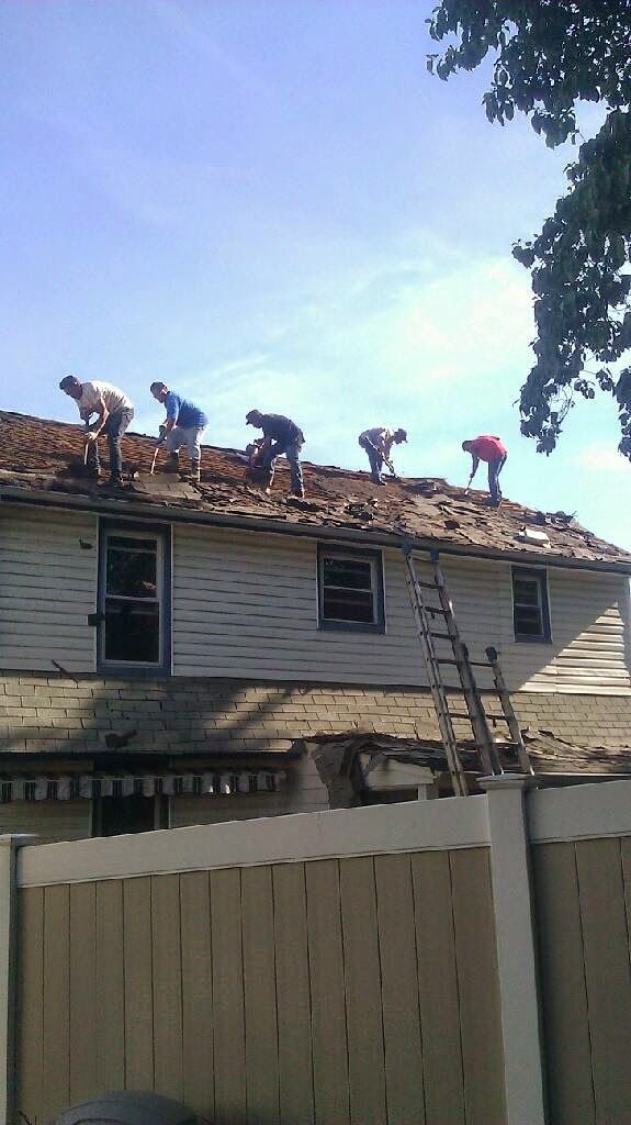 Five people working on a residential roof removal in front of a white house with a ladder leaning against it.