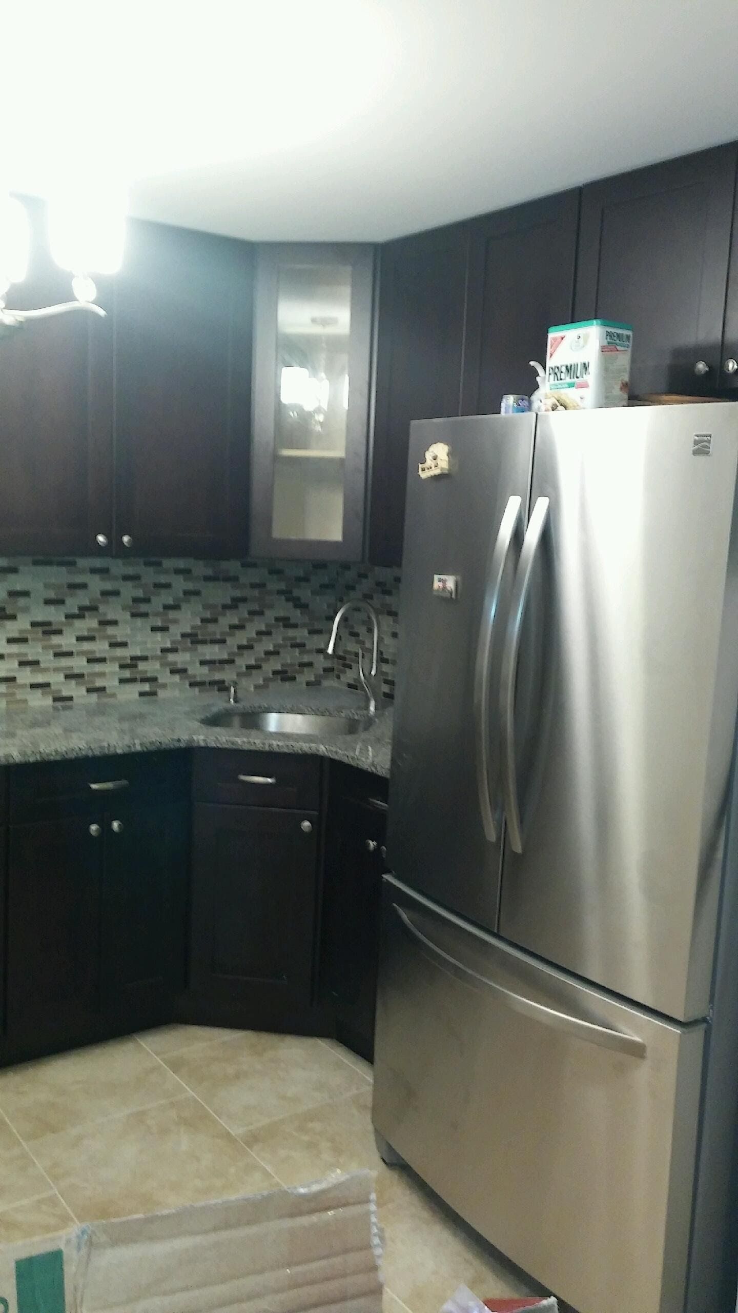 A modern kitchen corner featuring dark wood cabinets, a stainless steel refrigerator, and a speckled granite countertop.