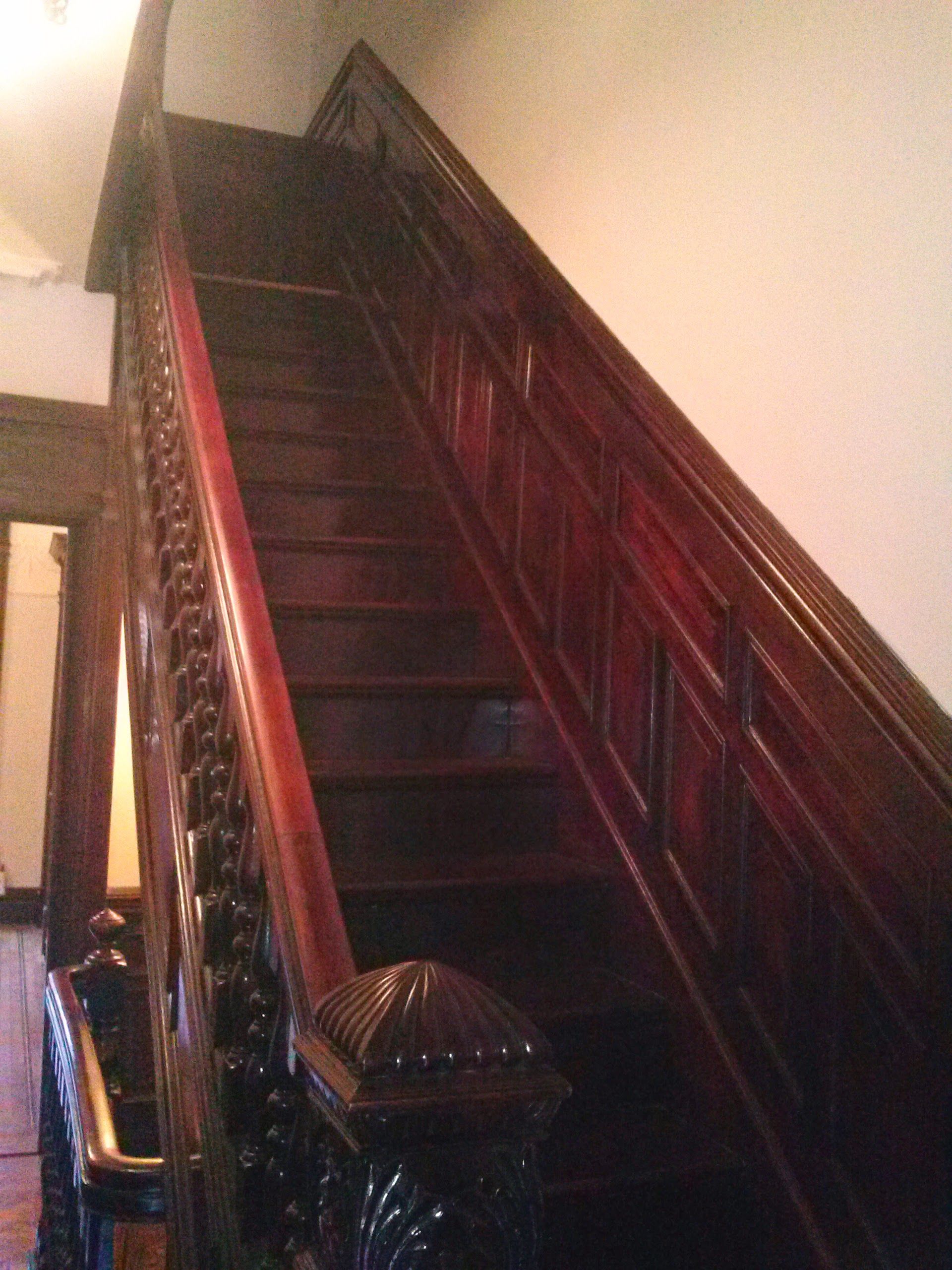 An ornate, dark wood staircase ascends steeply, featuring carved panels along the wall and an intricate balustrade.