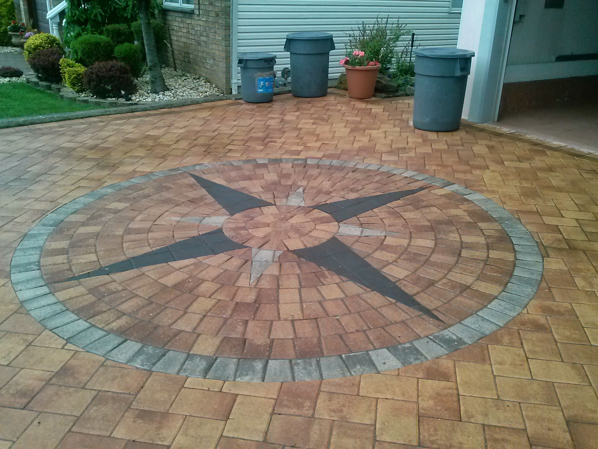 A paver driveway featuring a circular compass rose design with dark, star-shaped accents in shades of red and tan.