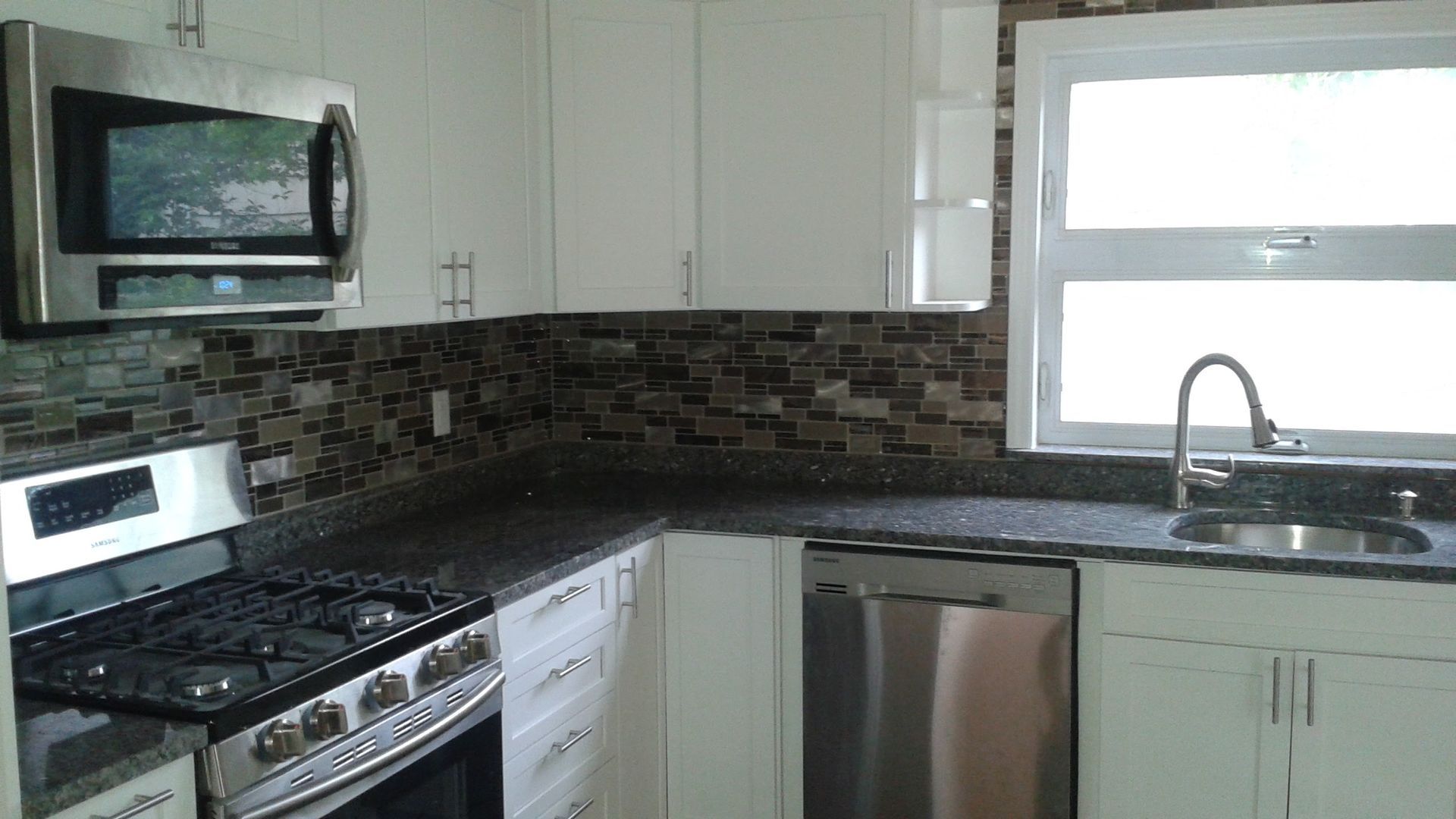 A modern kitchen featuring white cabinets, stainless steel appliances, dark countertops, and a stone tile backsplash.