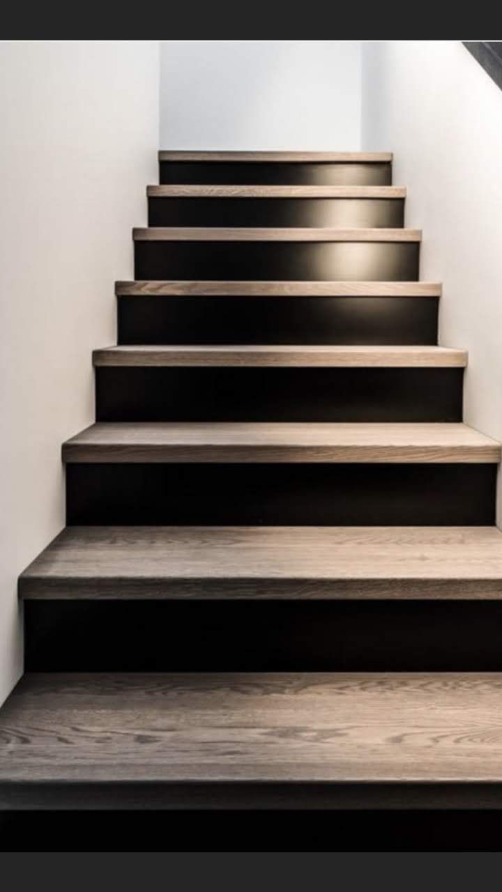 A straight, indoor staircase with dark wood treads and black risers, illuminated by soft lighting.
