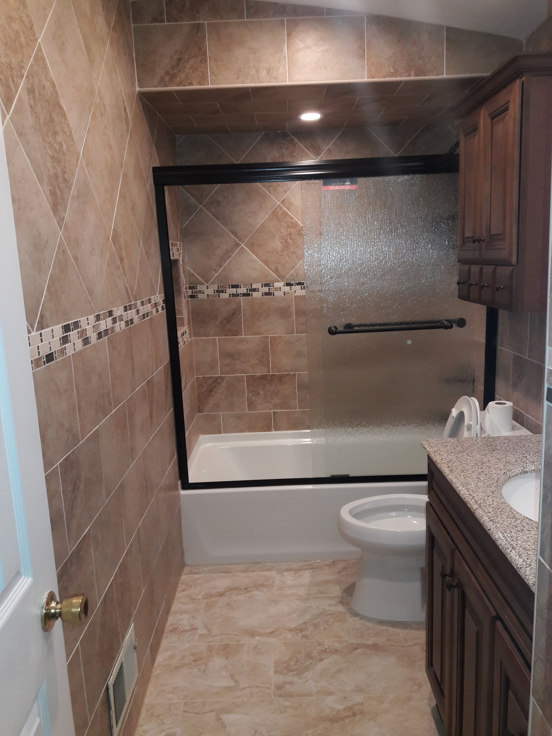 A bathroom with beige tile walls, a bathtub with sliding glass doors, a white toilet, and a dark wood vanity.